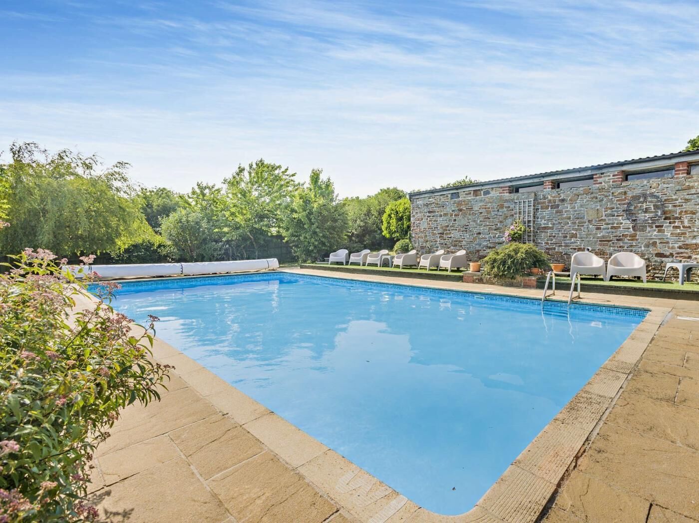 A rectangular swimming pool with a stone wall on one side and a grassy area with lounge chairs on the other.