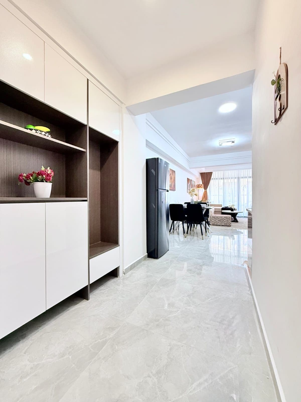 Una cocina moderna con armarios blancos, un refrigerador negro y un comedor con mesa y sillas.