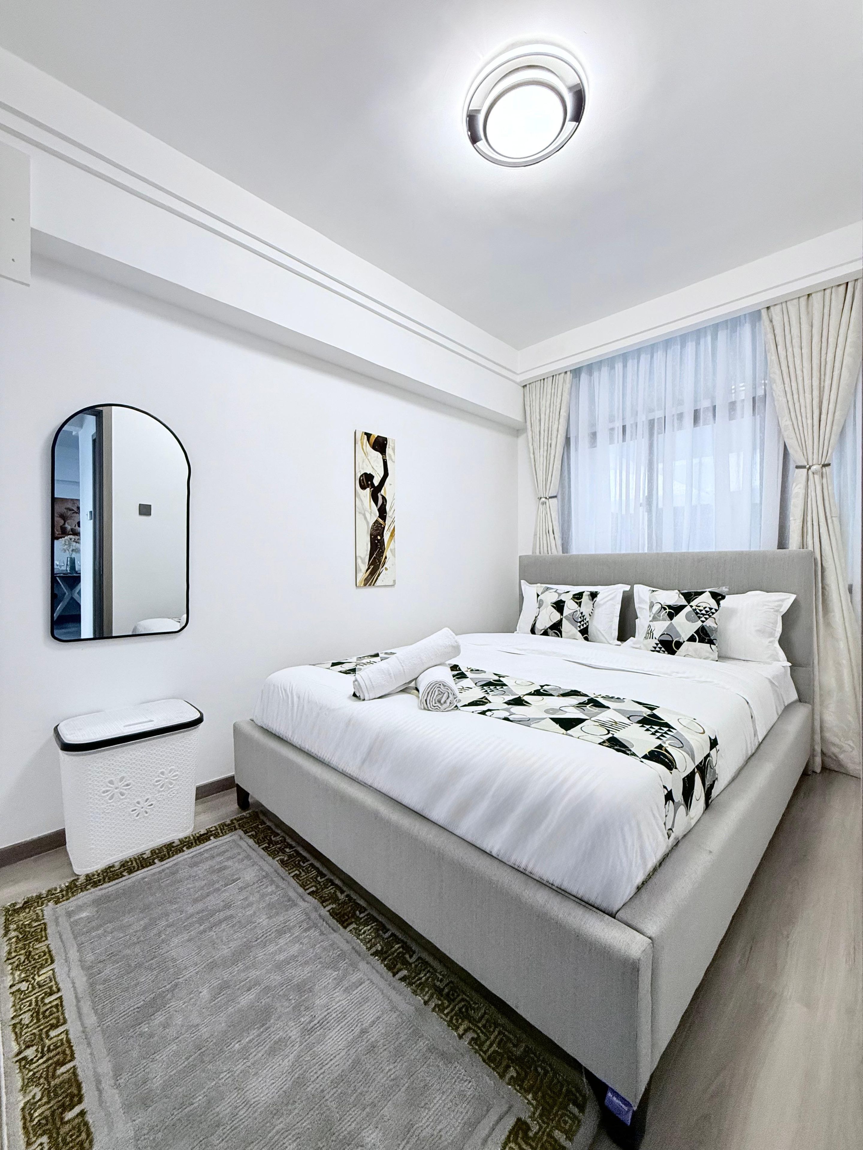 Un dormitorio moderno con una cama grande, un espejo de cabecera, una obra de arte en la pared y un lámpara del techo.