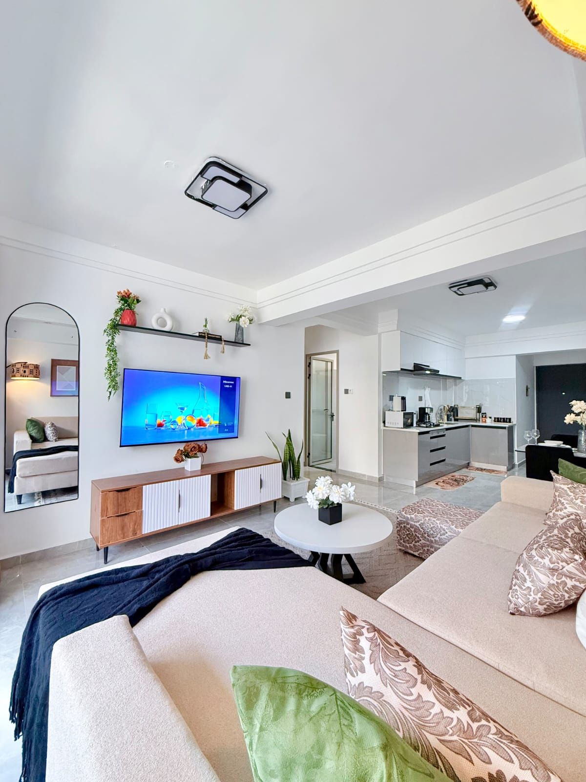 Een moderne woonkamer met een flatscreen televisie, een bank, een salontafel en een keuken in de achtergrond.