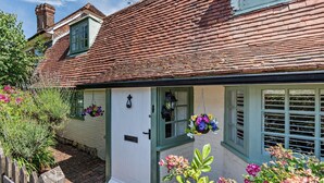 Ein traditionelles Cottage mit weißer Tür, grünen Fensterläden und blühenden Blumenkörben an der Fassade.