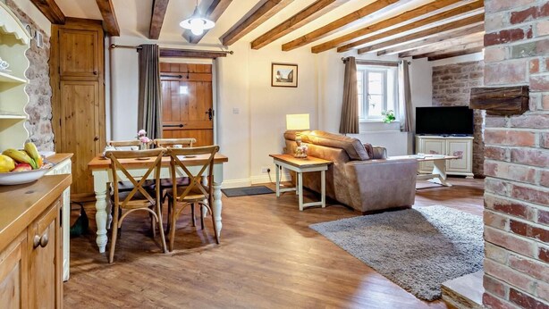 A cozy living room with wooden beams, a dining area with a wooden table and chairs, a sofa, a TV, and a fireplace. - 2 Bed in Nottingham (oc-47032) (Newthorpe)