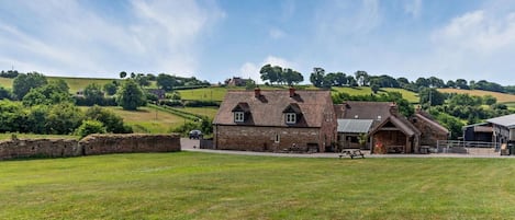 Un bâtiment rural doté d’une façade en pierre, d’une grange en bois et d’un champ verdoyant.