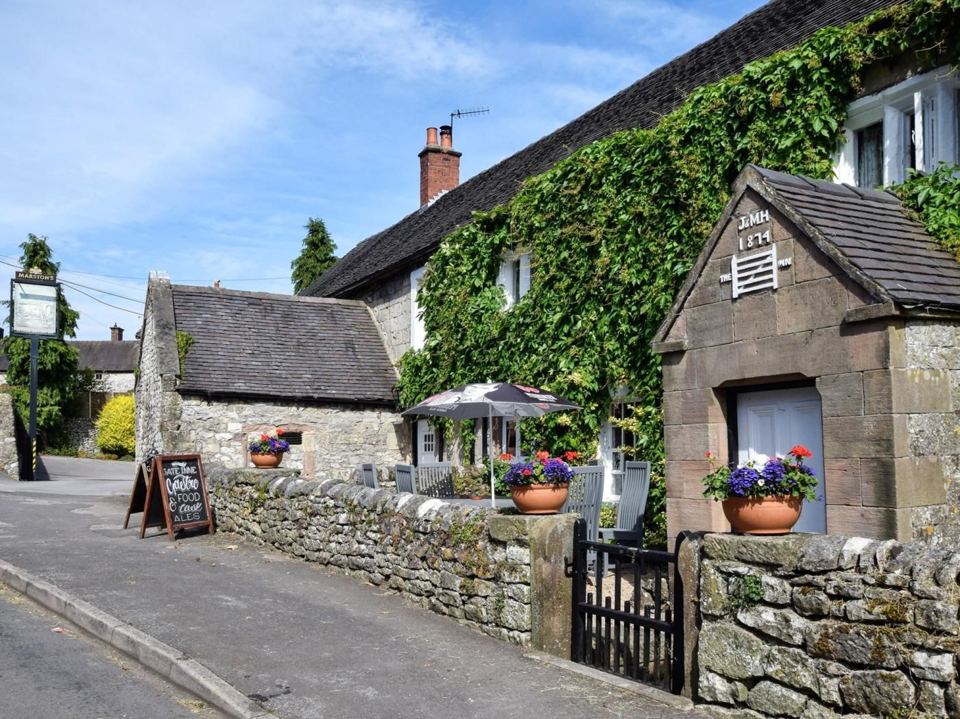 A stone building with ivy, a signboard, and outdoor seating with umbrellas.
