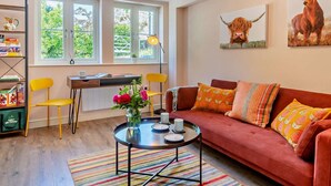 A cozy living room with a red sofa, a small round coffee table, a bookshelf, and a desk with a lamp. - 4 Bed in Matlock (oc-47450) (Brassington)