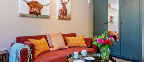 Una sala de estar con un sofá rojo, cojines coloridos, una mesa de centro con tazas y obras de arte con animales en la pared.