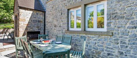 A stone building with a dining area featuring a table and chairs, a grill, and a window.