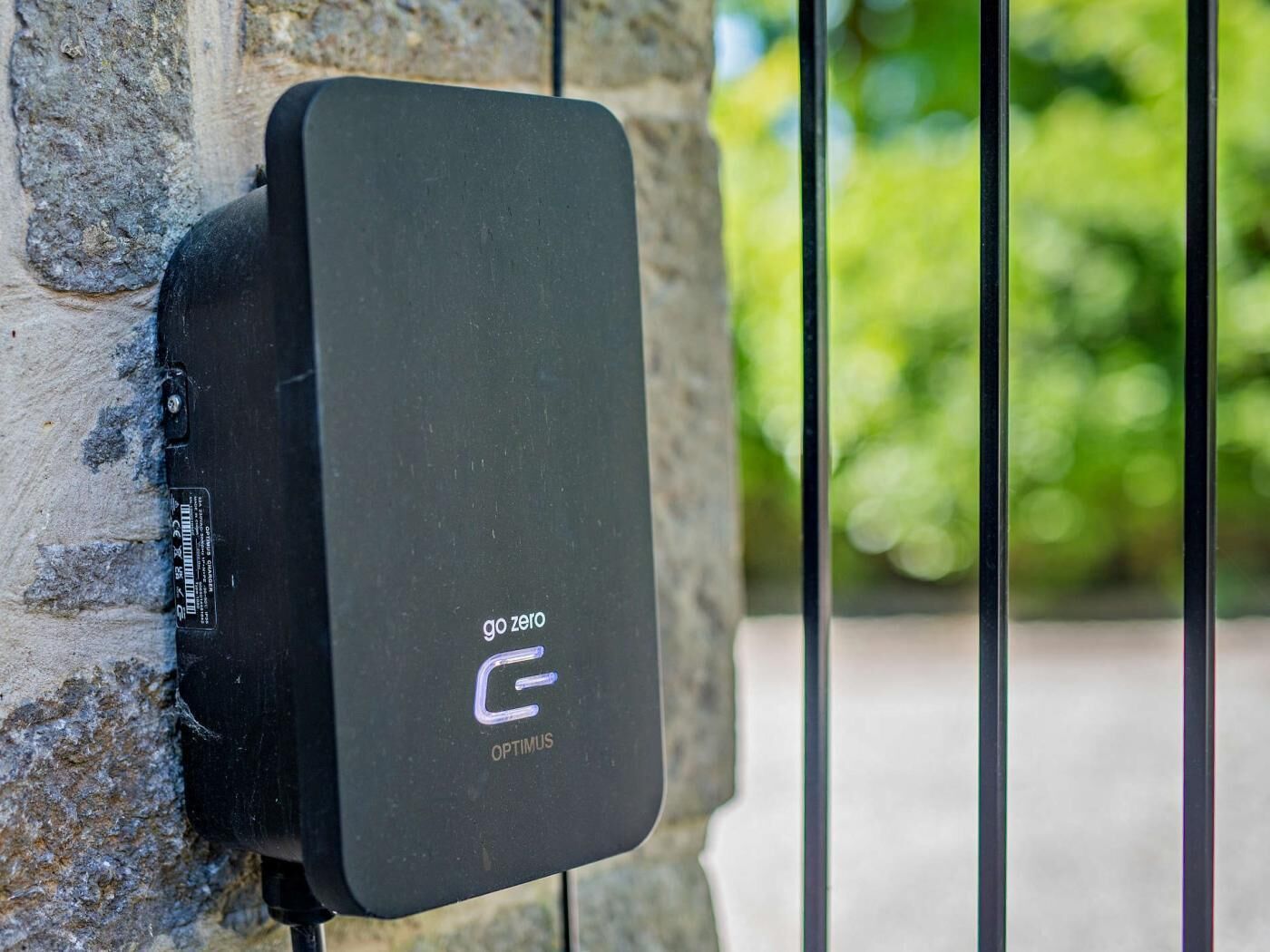 A black charging station labeled 'GO ZERO OPTIMUS' mounted on a stone wall.