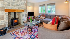A cozy living room with a stone fireplace, a sofa, a coffee table, and a TV. - 4 Bed in Matlock (oc-47450) (Brassington)