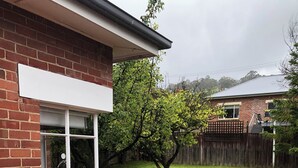 A residential backyard with a wooden deck, a brick house, a lawn, and a wooden fence.