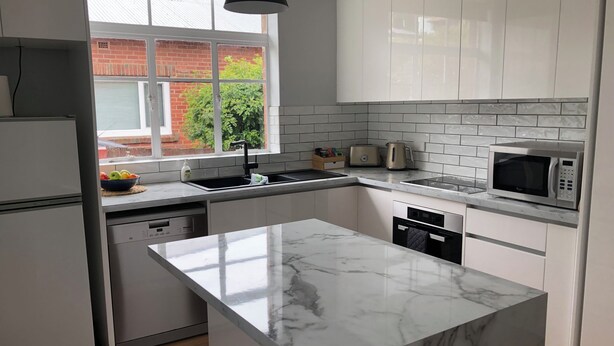 A modern kitchen with white cabinets, a marble island, a sink, a toaster, a kettle, and a microwave.
