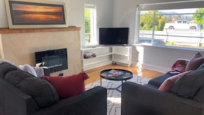 A living room with a fireplace, a flat-screen TV, two sofas, a coffee table, and a large window with a view of a white pickup truck.
