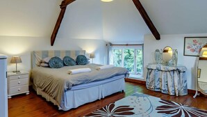 Ein Schlafzimmer mit einem Bett, Nachttischen, einer Kommode, einem Spiegel und einem Fenster mit Blick auf Grünfläche.