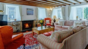 Ein gemütliches Wohnzimmer mit Kamin, gestreiften Sofas, einem roten Teppich mit Muster und Holzbalken an der Decke.