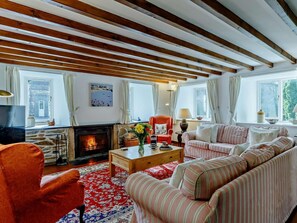 Ein gemütliches Wohnzimmer mit Kamin, gestreiften Sofas, einem roten Teppich mit Muster und Holzbalken an der Decke.