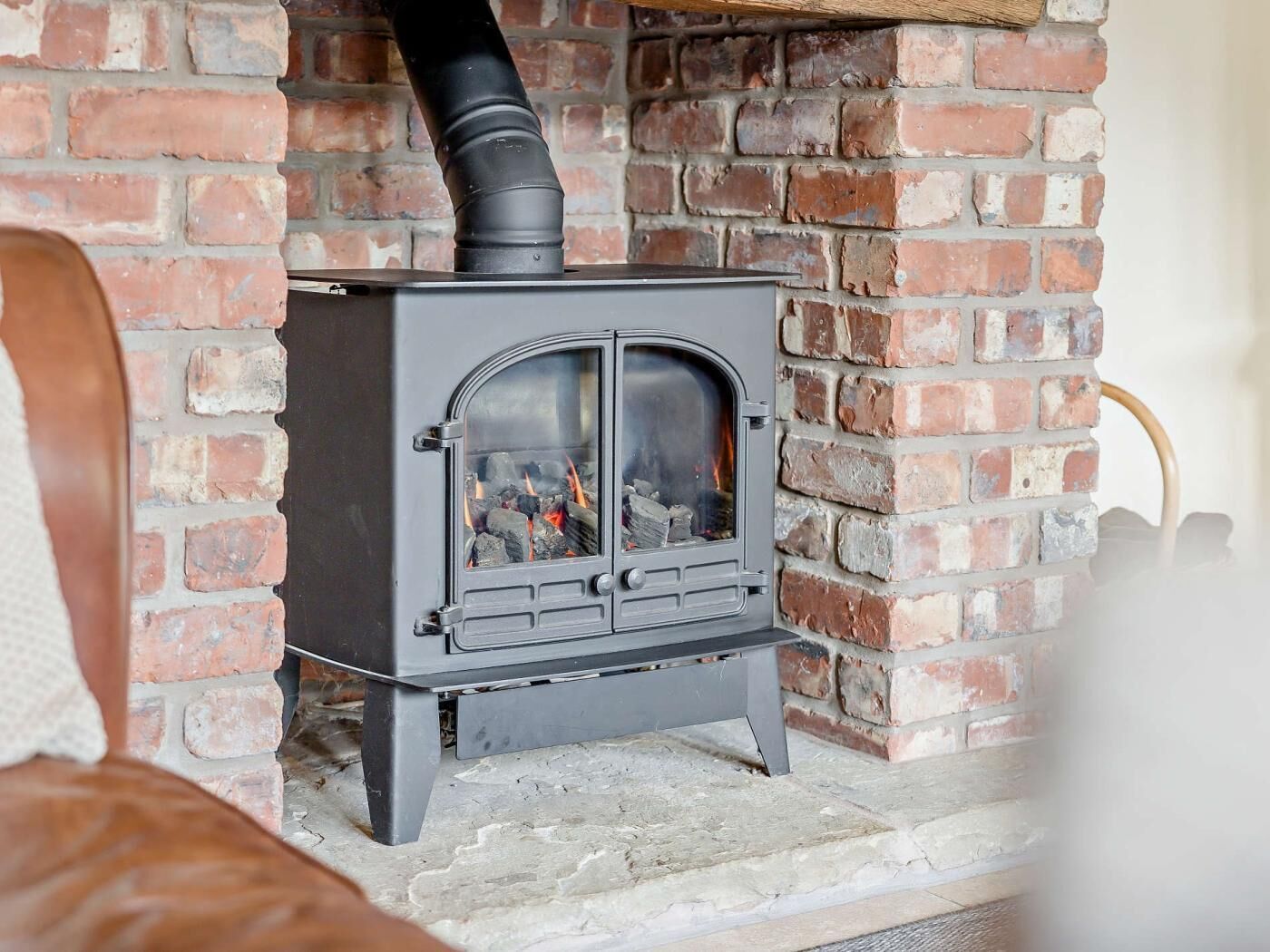 A wood-burning stove with a chimney, set against a brick wall.