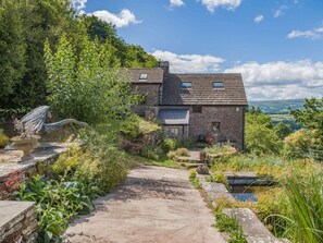 A stone house with a sloped roof, a garden with a pond, and a view of the countryside. - 1 Bed in Crickhowell (oc-48082) (Llanbedr)