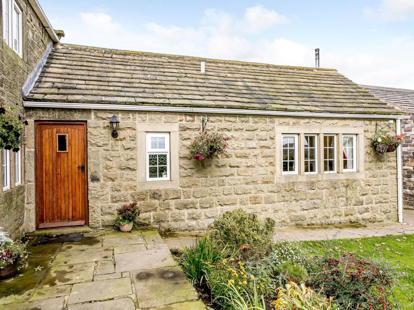 A stone cottage with a wooden door, two windows, and a small garden with potted plants.