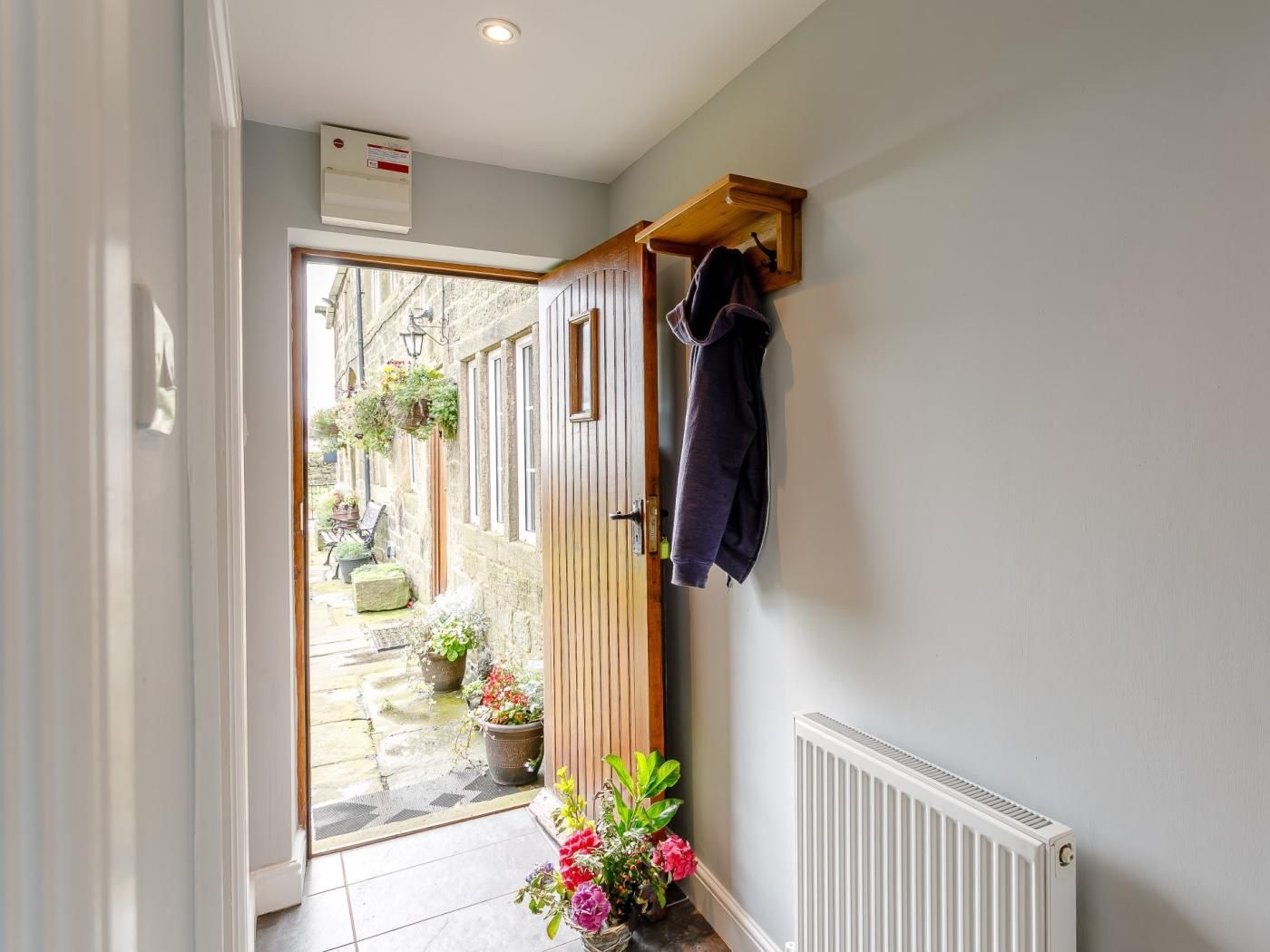 Un couloir étroit avec une porte en bois donnant sur un espace extérieur agrémenté de plantes en pot et d’un banc.