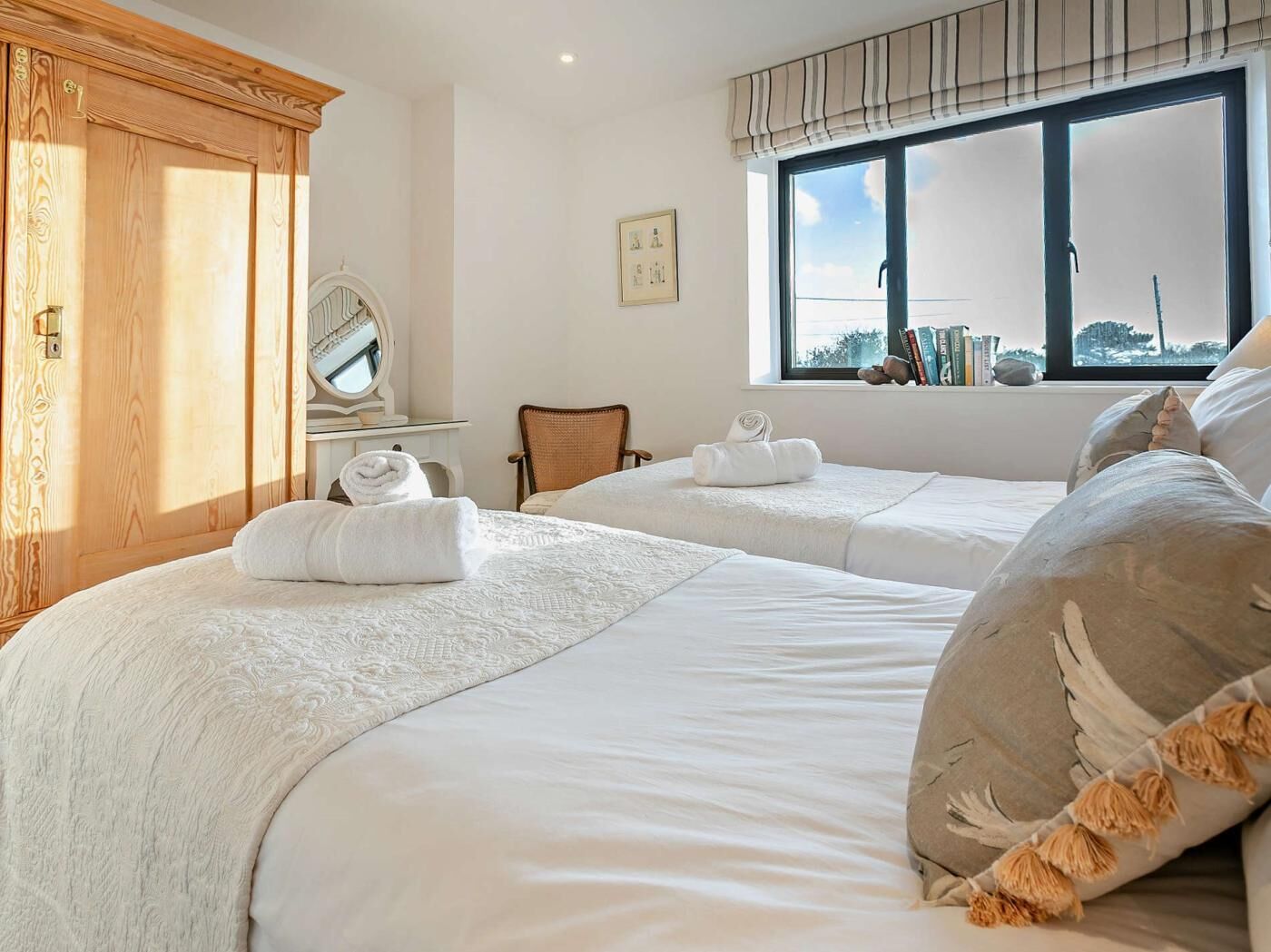 Une chambre d’hôtel avec deux lits, une armoire en bois, un miroir, une fenêtre donnant sur un beau paysage et une chaise.