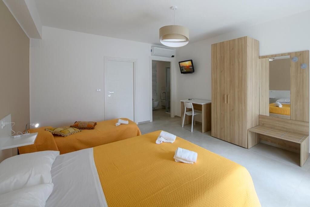 A hotel room with two beds, a desk, a chair, a wardrobe, and a television.