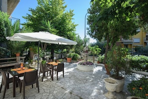 Un espace extérieur aménagé en terrasse, avec un sol en pierre, des tables, des chaises et des parasols.