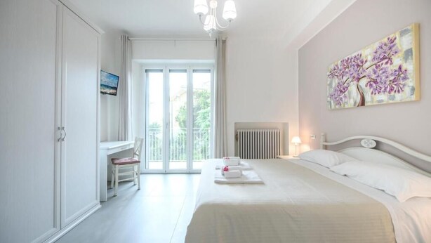 A bedroom with a bed, a desk, a chair, a radiator, and a painting on the wall.