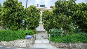 A gated entrance with a stone wall, a metal gate, and a building with a flat roof and balconies.