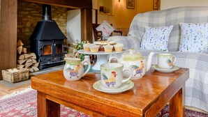 A cozy room with a fireplace, a sofa, a table with teacups and a tray of cupcakes, and a wicker basket. - 2 Bed in Cirencester (oc-48925) (Daglingworth)