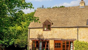 A stone building with a pitched roof, a central window with a triangular pediment, and a door with a wooden frame. - 2 Bed in Cirencester (oc-48925) (Daglingworth)