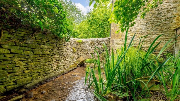 A narrow stone pathway with a small stream, surrounded by lush greenery and a stone wall. - 2 Bed in Cirencester (oc-48925) (Daglingworth)