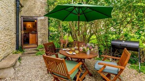 An outdoor patio with a round wooden table, four wooden chairs, a green umbrella, and a barbecue grill. - 2 Bed in Cirencester (oc-48925) (Daglingworth)