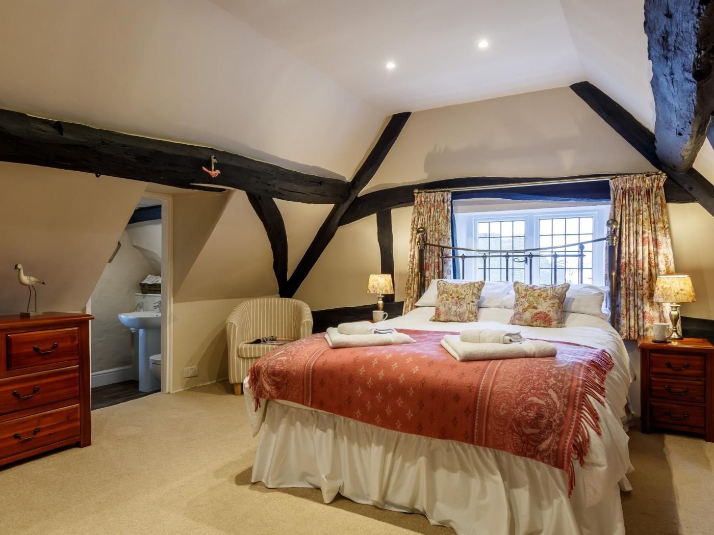 Een slaapkamer met een groot bed, een stoel, een dressoir en een raam met gordijnen.