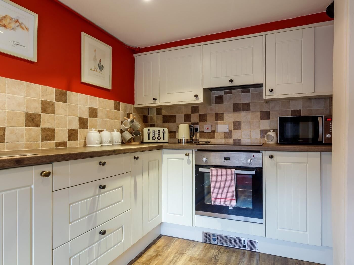 Une cuisine avec des meubles blancs, un four à micro-ondes, une bouilloire et un mur rouge.