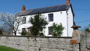 A white cottage with a stone wall, solar panels, and a sign reading 'May Blossom Cottage.' - 1 Bed in Taunton (oc-49569) (North Curry)
