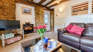 Una sala de estar acogedora con pared de piedra, chimenea, televisor y sofá de cuero.
