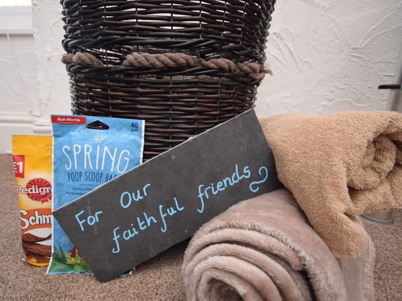 A wicker basket, a blue package labeled 'SPRING,' a brown towel, and a chalkboard sign with 'For Our faithful friends' written on it.