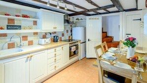 Una cocina con gabinetes blancos, salpicadero de azulejos, un lavamanos, un tostador y una zona de comedor con una mesa preparada para dos.