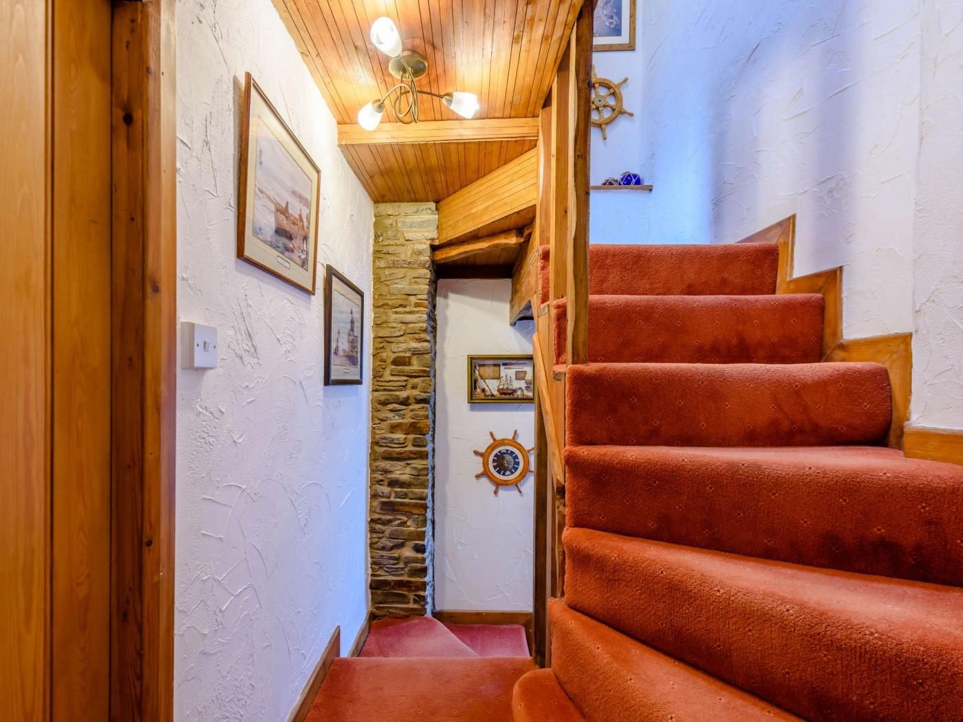 A wooden staircase with red carpeted steps leading to a room with a stone wall and a wooden ceiling.
