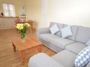A living room with a grey sofa, wooden coffee table, and a vase of flowers. - 1 Bed in North Walsham (oc-49722) (Worstead)