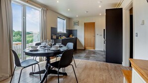 Uma sala de jantar com uma mesa posta para quatro, cozinha ao fundo e vista para o exterior.