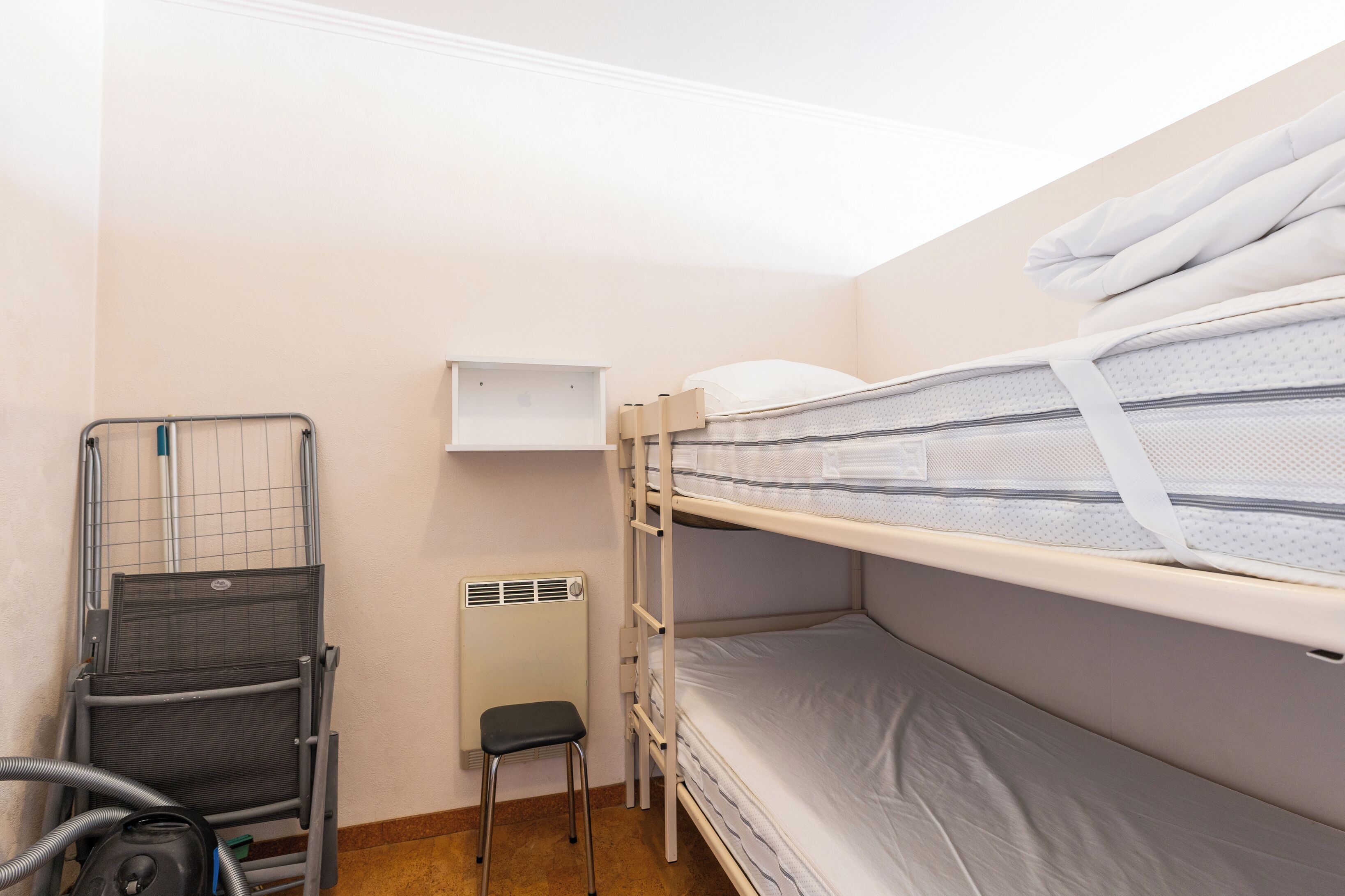 Une chambre avec un lit superposé, une structure en métal, un radiateur et un petit tabouret.