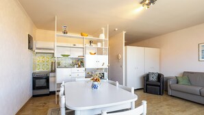 Ein kompakter Wohnbereich mit Esstisch, Stühlen, einer Sitzecke und einer Küchenzeile inklusive Backofen und Kühlschrank.