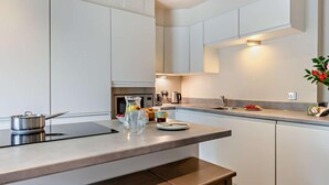 Uma cozinha moderna com armários brancos, uma ilha central, forno embutido e máquina de café.