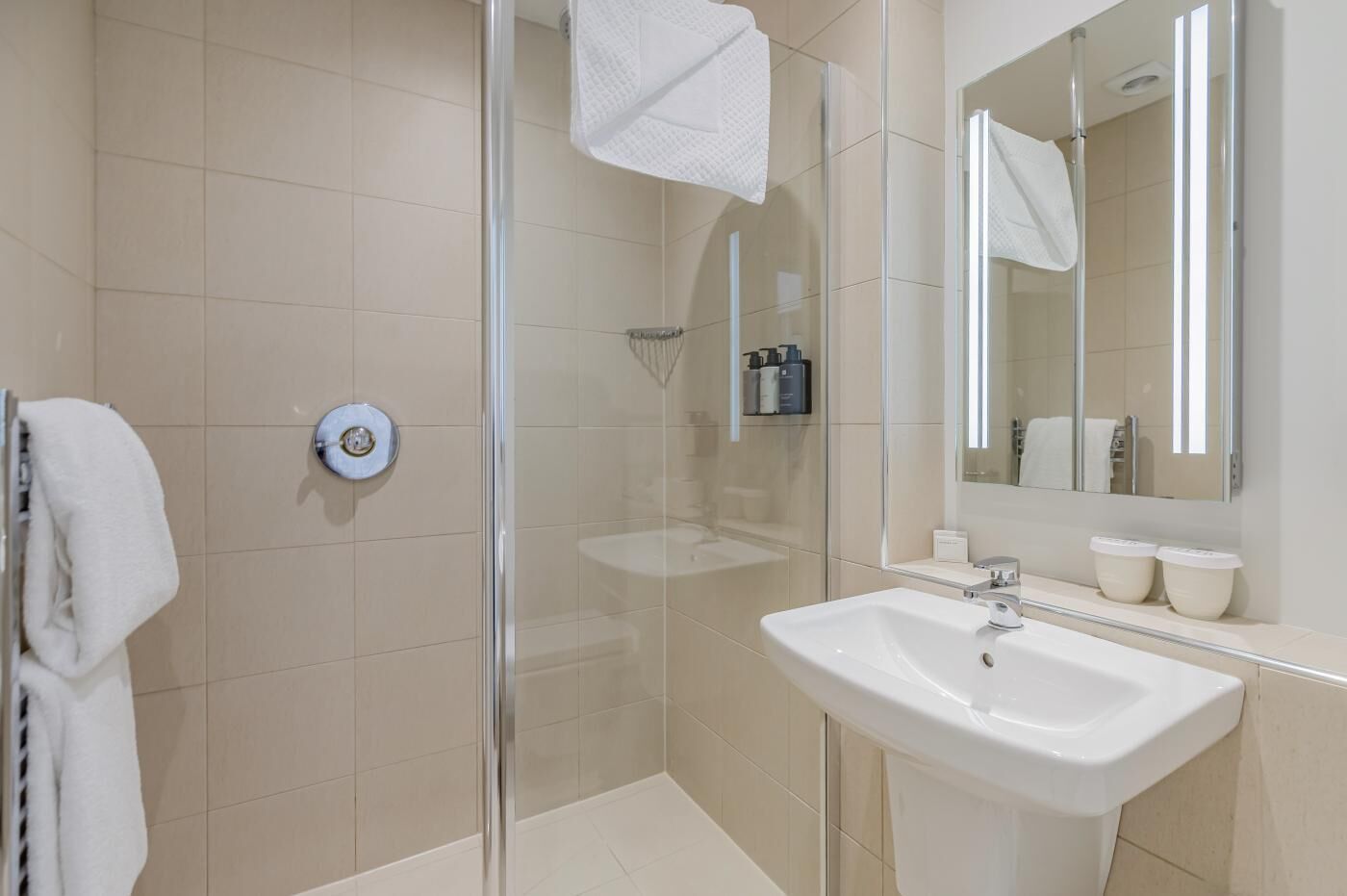 Un baño moderno con cabina de ducha de vidrio, un lavabo blanco y un espejo grande.