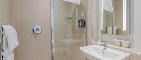 Un baño moderno con cabina de ducha de vidrio, un lavabo blanco y un espejo grande.