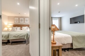 A hotel room with two beds, a flat-screen TV mounted on the wall, and a small table with a lamp. - 2 Bed in Saundersfoot (oc-50576) (Saundersfoot)
