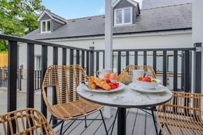 A balcony with wicker chairs, a round table, and breakfast items including croissants, eggs, and strawberries. - 2 Bed in Saundersfoot (oc-50576) (Saundersfoot)