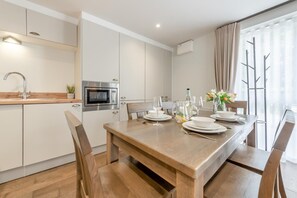 Una cucina moderna con forno integrato e microonde, tavolo da pranzo in legno per quattro persone e una grande finestra con tende.