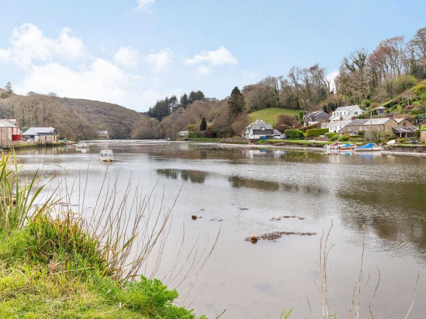 A river with boats, houses along the banks, and a hilly landscape in the background.